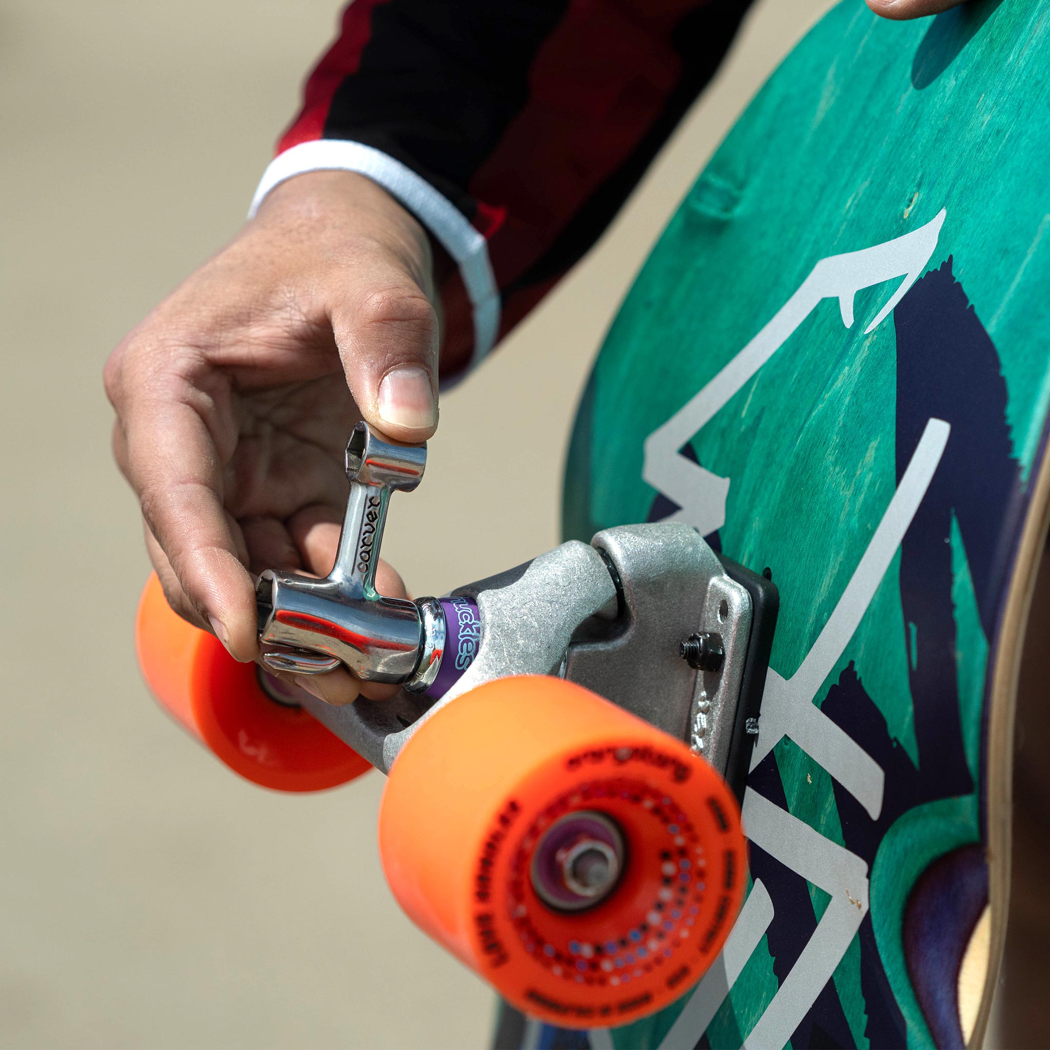 Close-up of a hand adjusting a skateboard wheel with a colorful board in the background.