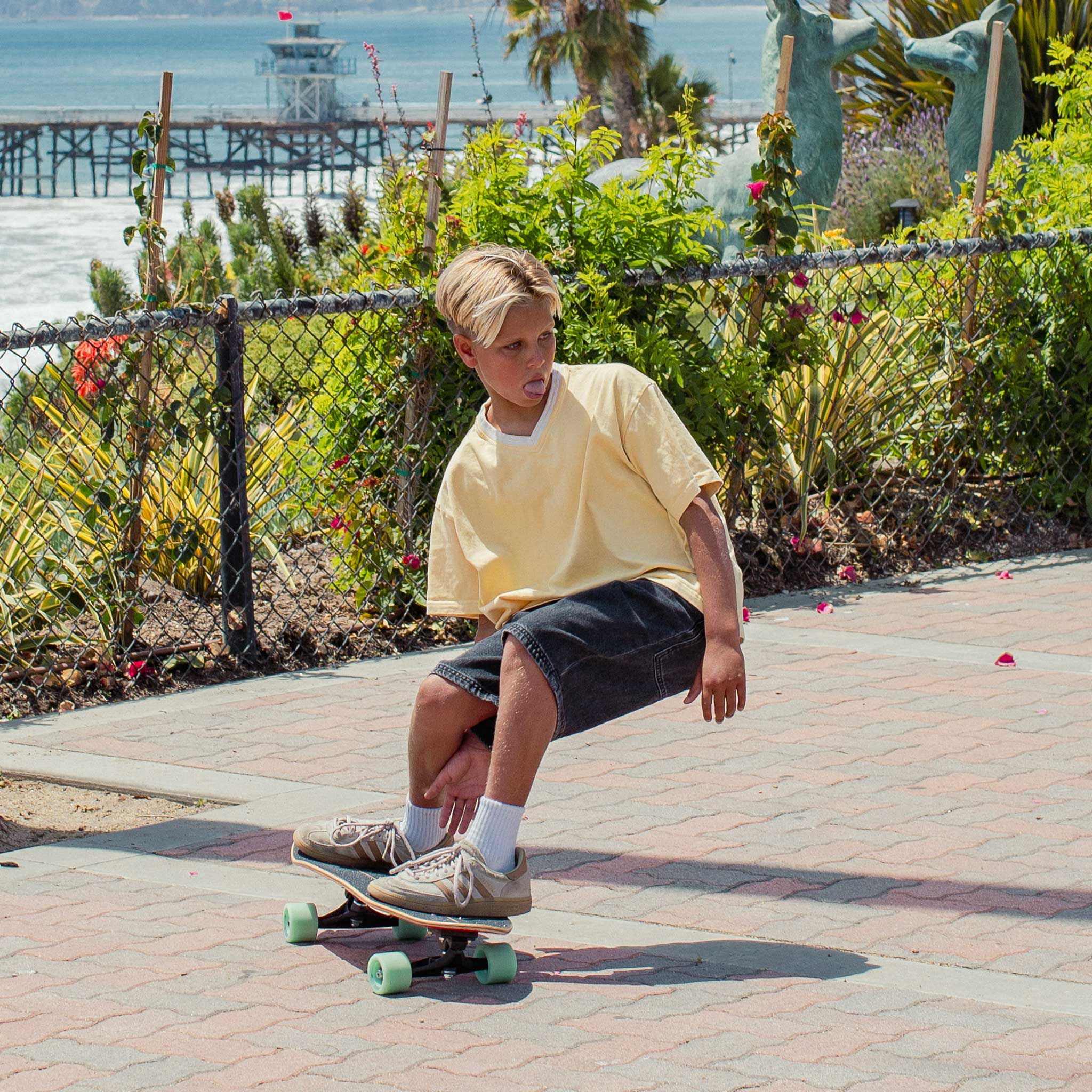 Child skateboarding on Carver Wavy Davy mini surfskate on a sidewalk with a beach and pier in the background