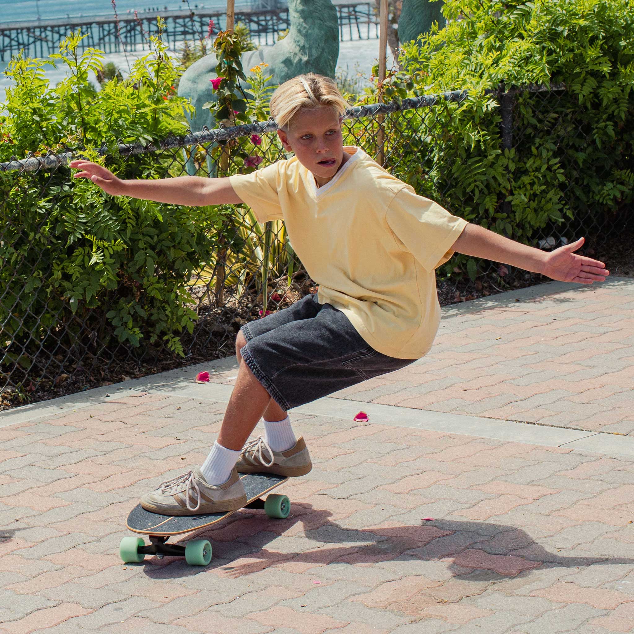 Person skateboarding on Carver Wavy Davy mini surfskate on a paved path with greenery and a fence in the background