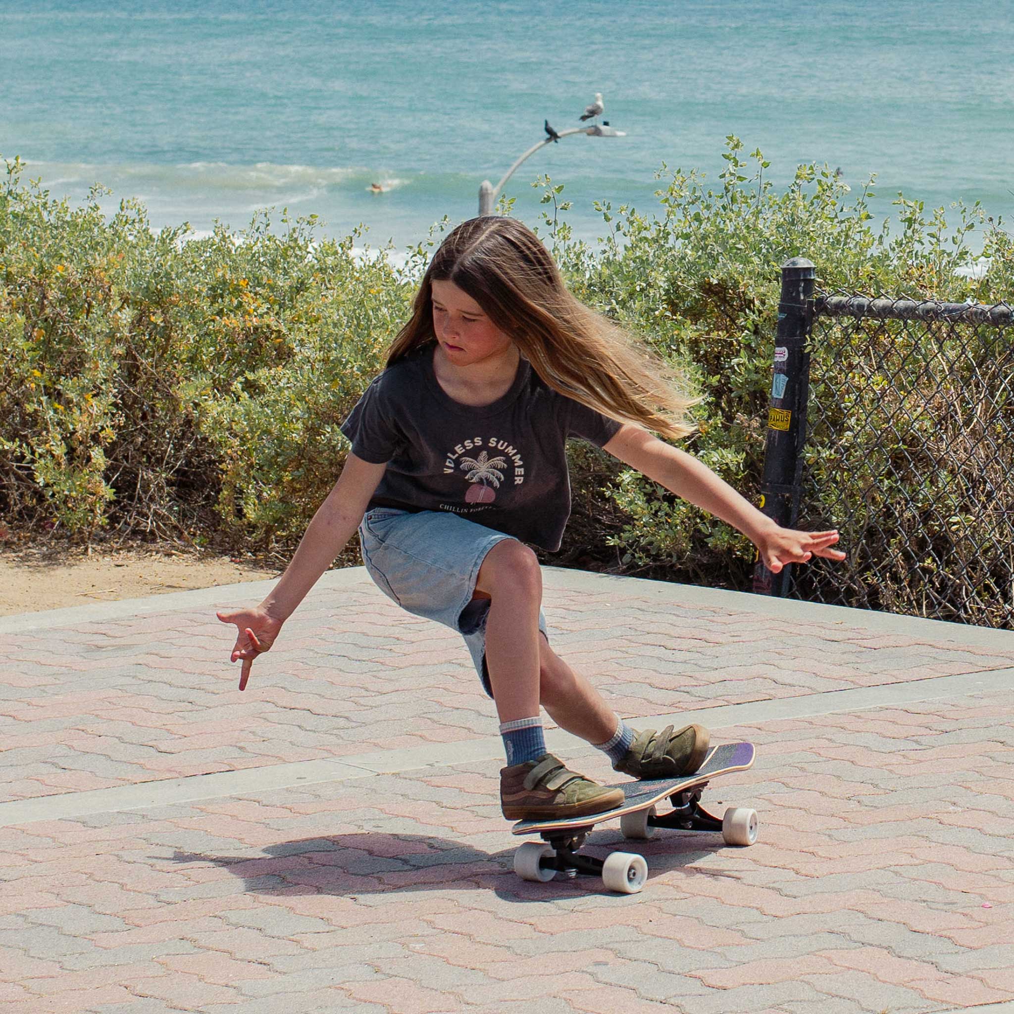 Child skateboarding on Carver Purple Haze mini surfskate on a paved path by a body of water