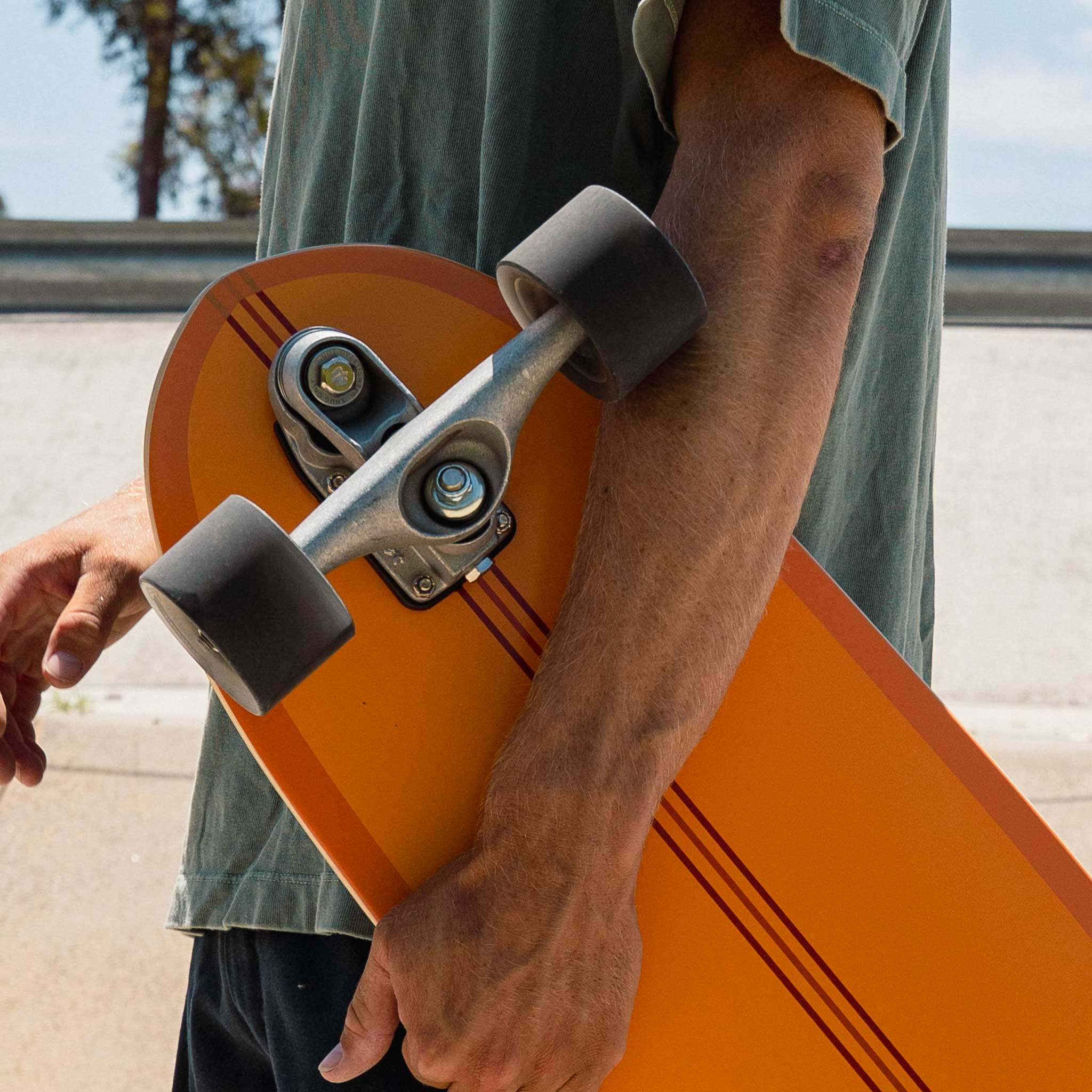Person holding an orange Carver CI Noserider surfskate skateboard with a blurred background