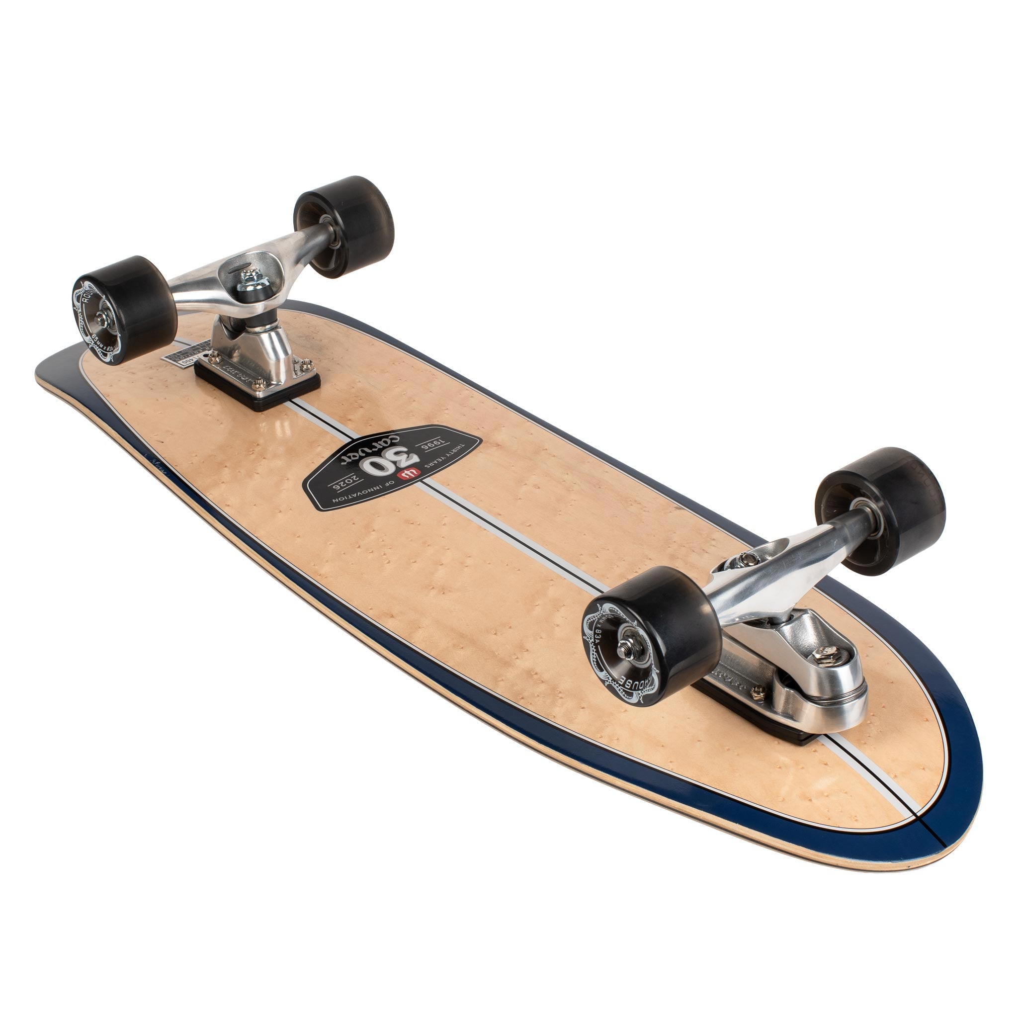 A Carver 30-Year Limited Edition surfskate skateboard shown from an angled top-down view on a white background. The deck has a natural light wood grain finish with a dark navy blue border and a thin white center stripe.