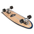 A Carver 30-Year Limited Edition surfskate skateboard shown from an angled top-down view on a white background. The deck has a natural light wood grain finish with a dark navy blue border and a thin white center stripe.
