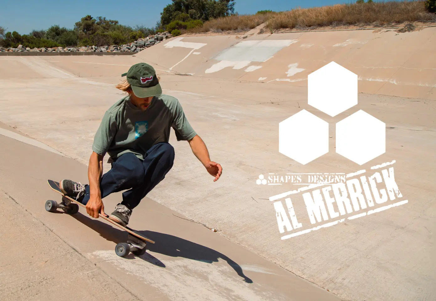 A person skateboarding in a concrete bowl at a sunny outdoor skatepark, wearing a green cap, olive green t-shirt, and dark blue jeans. A large white graphic overlay on the right features three hexagons and the text 'SHAPE DESIGNS AL MERRICK'.