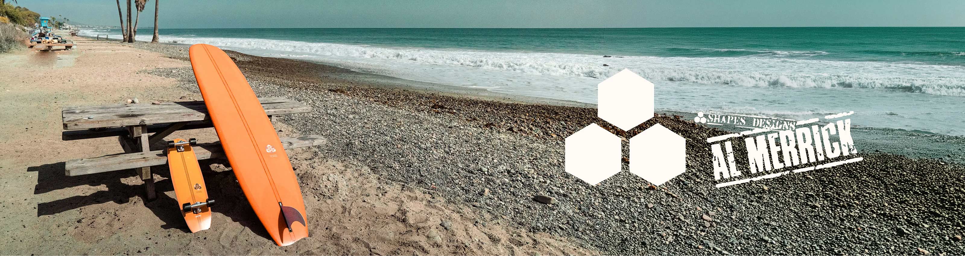 An orange surfboard and matching orange longboard skateboard rest on a beach picnic table on a sandy shoreline with pebbles and the ocean in the background. The Channel Islands Al Merrick logo is visible on the right side of the image.