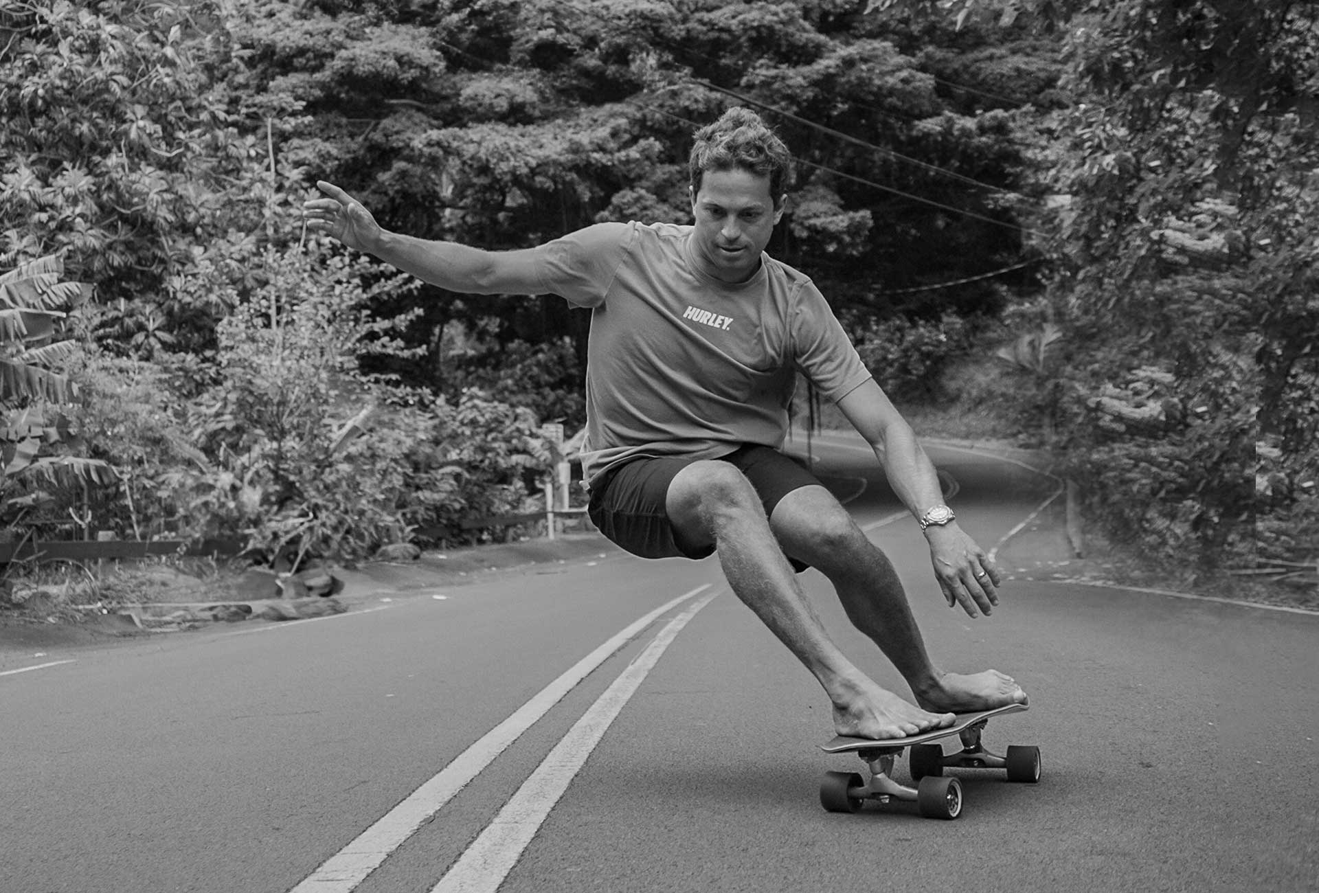Carver team rider Kai Lenny skateboarding on a road with trees in the background