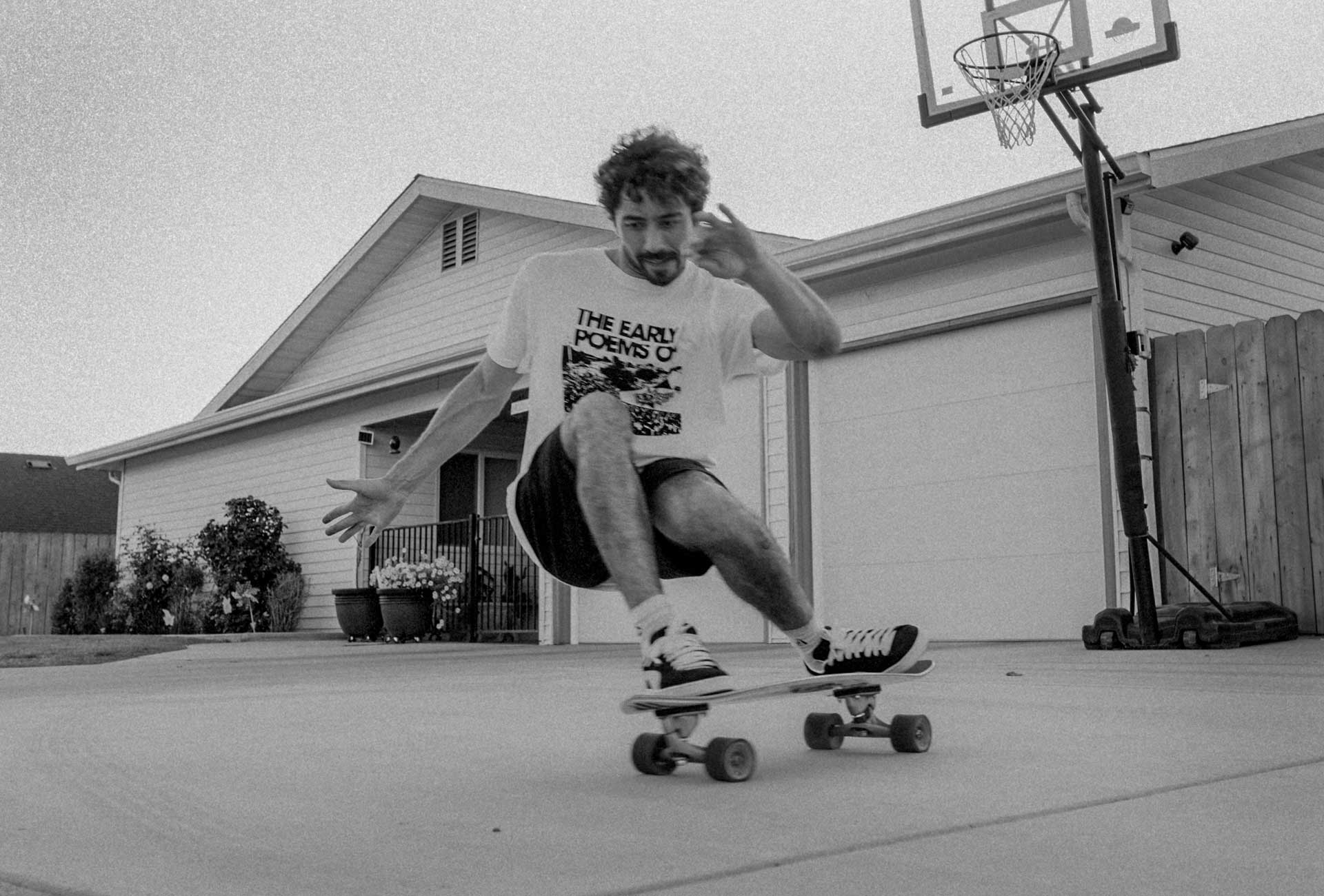 Carver team rider Yago Dora skateboarding in a driveway with a house and basketball hoop in the background