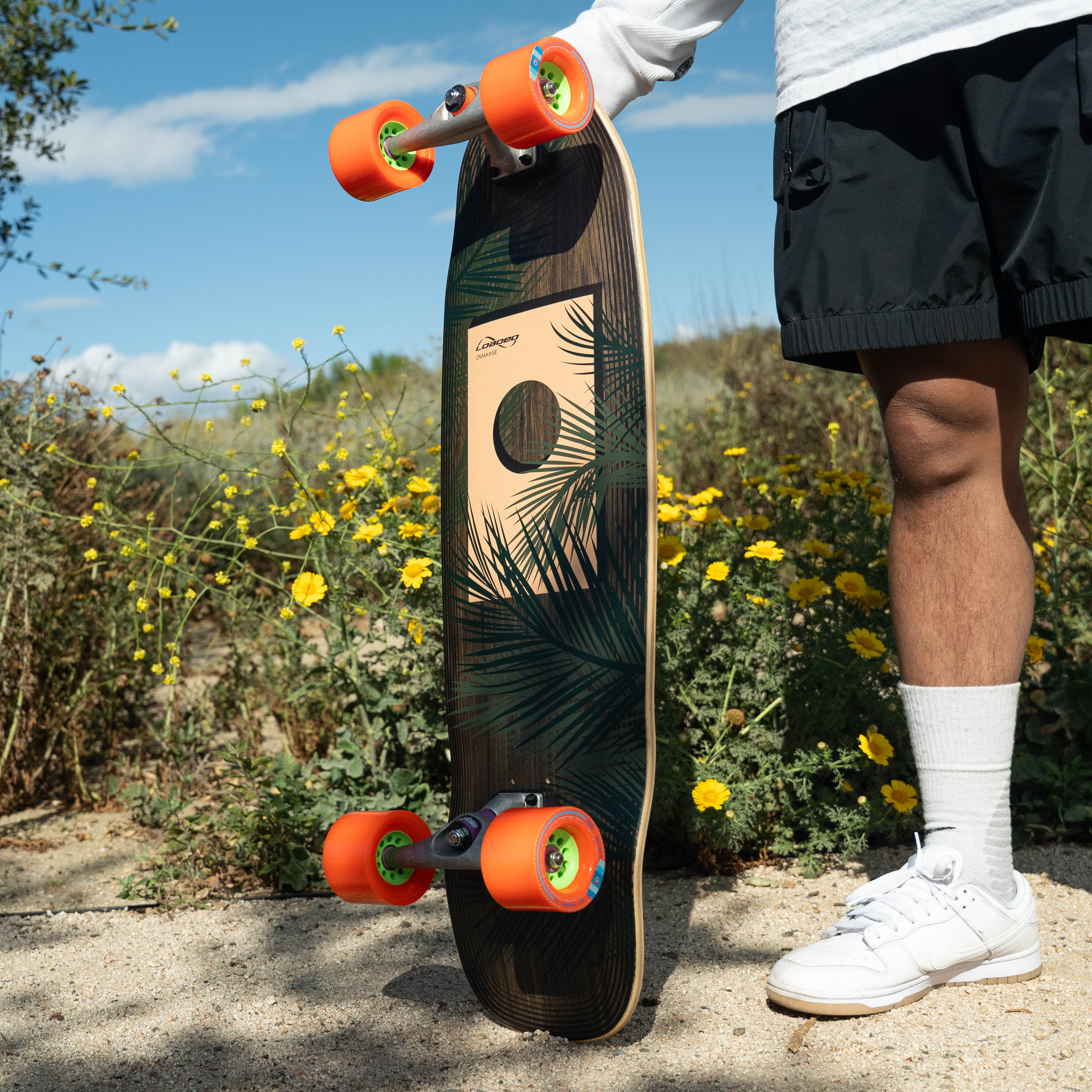 Person holding Loaded Omakase skateboard with a floral design in a natural setting